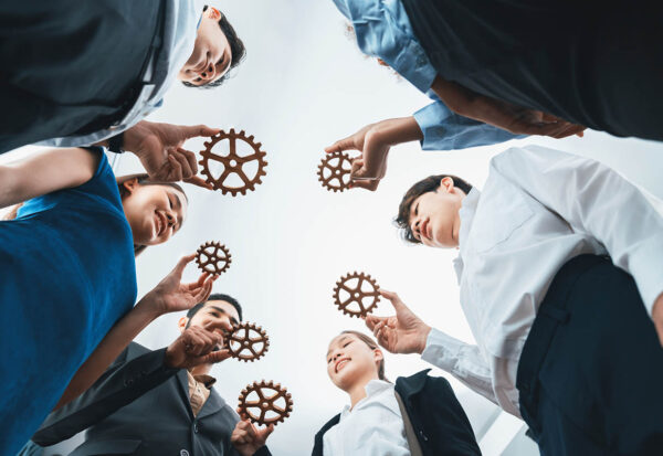 Below view office worker holding cog wheel as unity and teamwork in corporate workplace concept. Diverse colleague business people as symbol of visionary system teamwork for business success. Concord